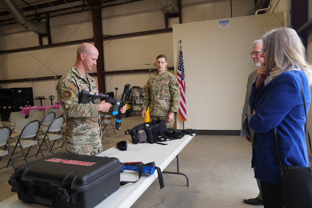 A man in a military uniform demonstrates the use of a weapon to a woman in civilian clothing.