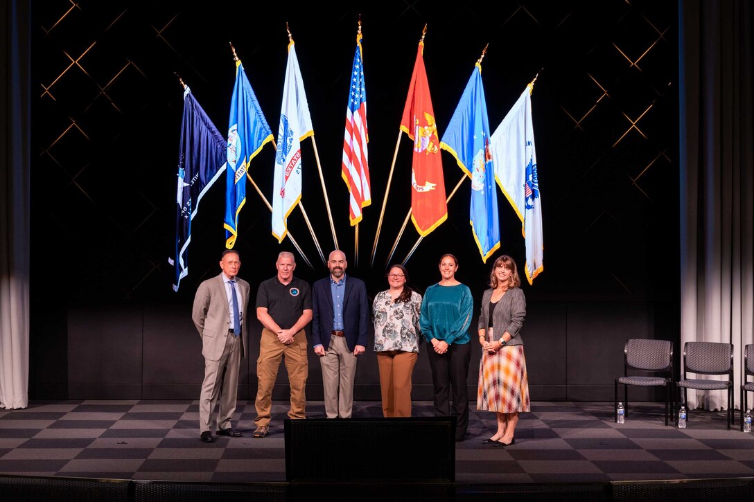 Civilians wearing business attire pose for a photograph on a stage.