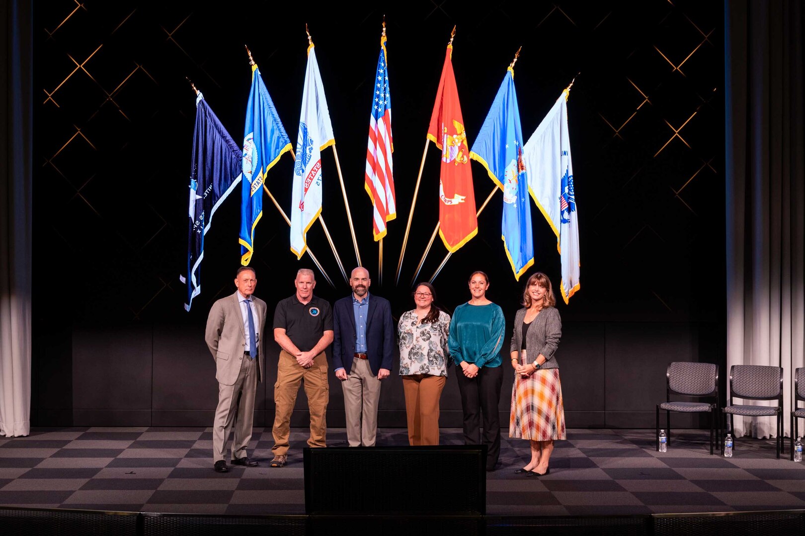 Civilians wearing business attire pose for a photograph on a stage.