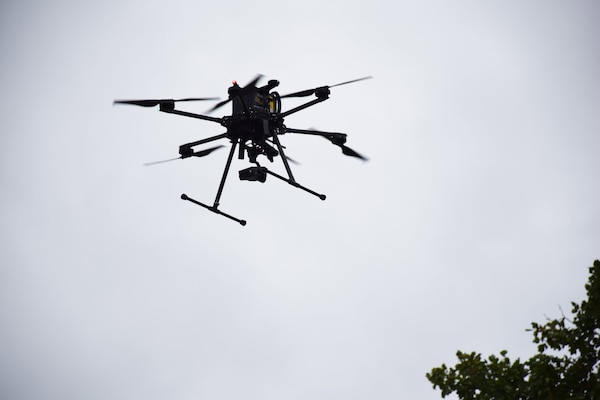 A drone with six propellers hovers in the overcast sky.
