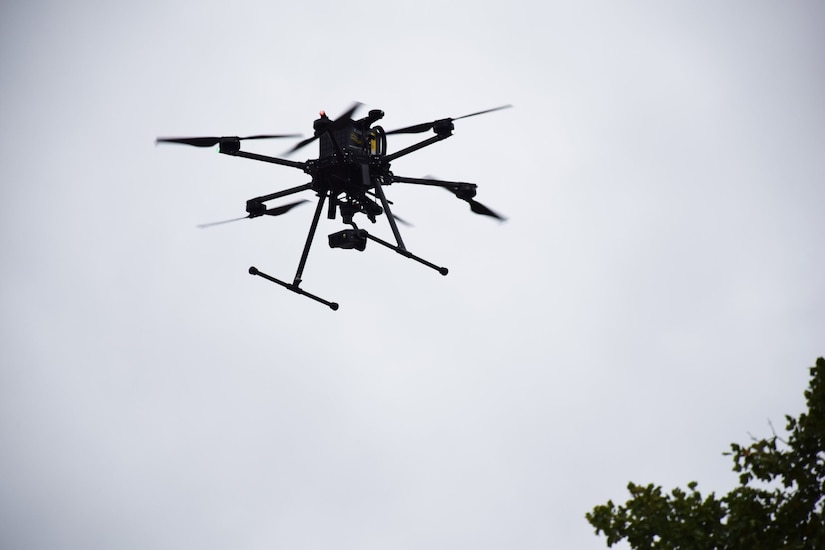 A drone with six propellers hovers in the overcast sky.