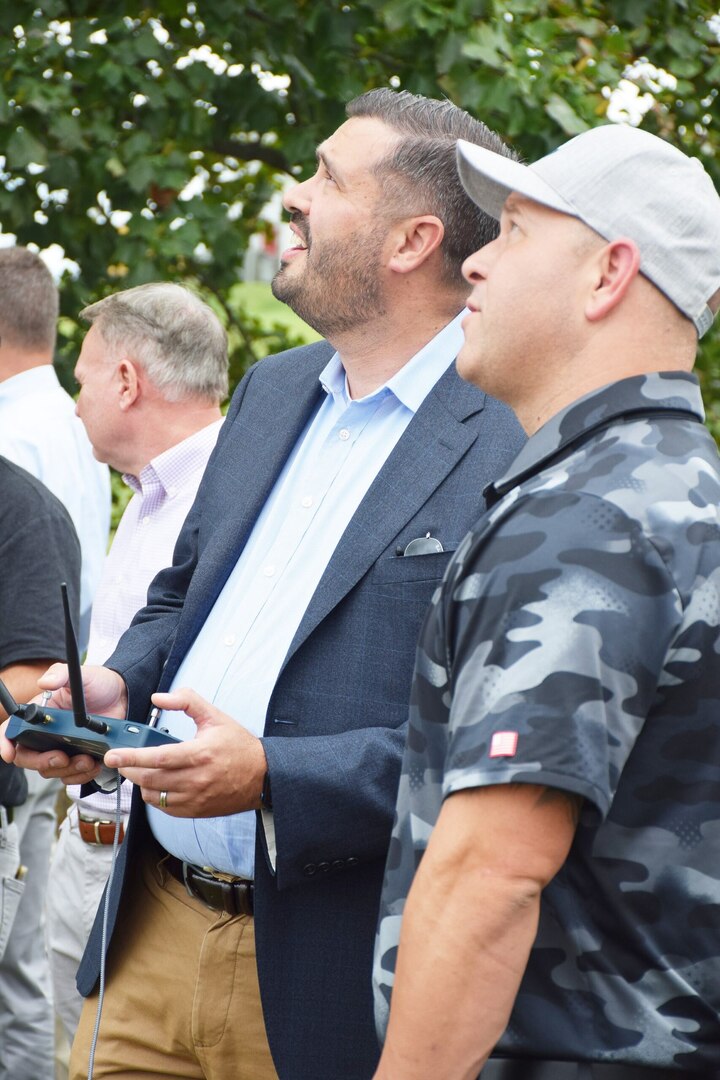 Two men standing together gaze skyward. One man is operating a remote control.