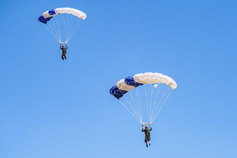 Two people wearing parachutes float downward.