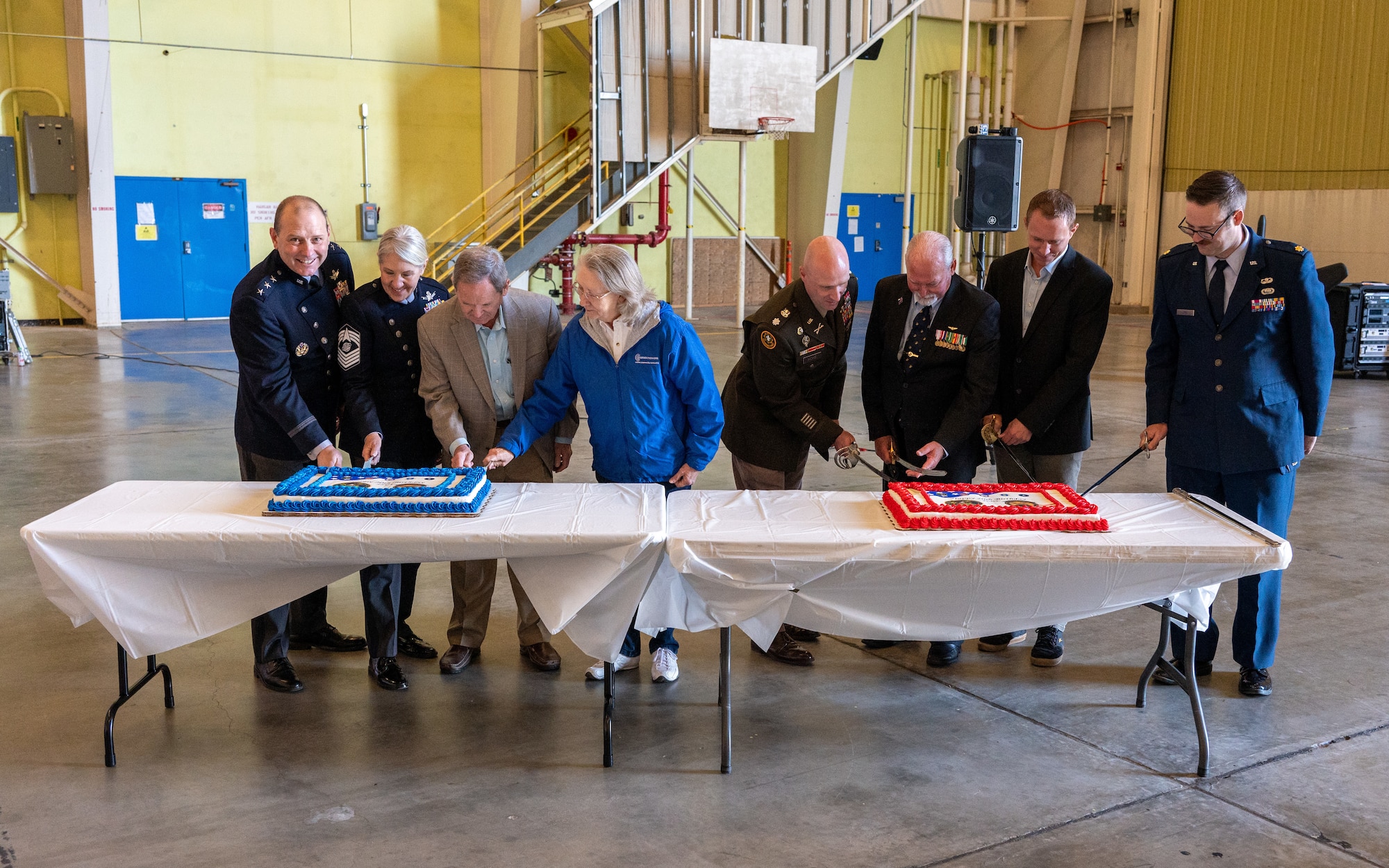 A group of people cut two cakes at a table during a ceremony.