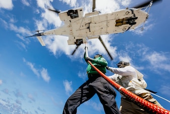 LSC Antonio Evans, right and LS3 Devon Smith hook supplies onto an AS-332 Super Puma helicopter from USNS Cesar Chavez (T-AKE 14) aboard USS George Washington (CVN 73) in the Pacific Ocean.