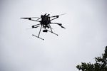 A drone with six propellers hovers in the overcast sky.