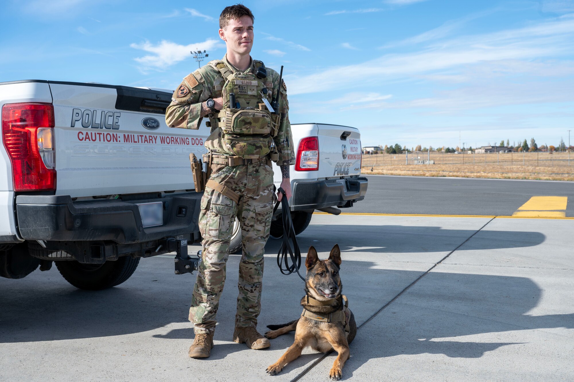 U.S. Air Force Senior Airman Lane Steed, a military working dog handler, assigned to the 92nd Security Forces Squadron, stands with MWD Sipo during exercise Mobility Response 25 in support of U.S. Strategic Command exercise Global Thunder 25 at Fairchild Air Force Base, Washington, Oct. 20, 2024. Sipo awaited a command to begin clearing the area of potential explosive devices. Mobility Response is an opportunity for Mobility Air Force to test their ability to respond to and simultaneously support multiple combatant commander’s requirements, such as USSTRATCOM’s reliable strategic deterrence force. (U.S. Air Force photo by Airman 1st Class Samantha Thorn) (This photo has been altered by blurring for operational security.)