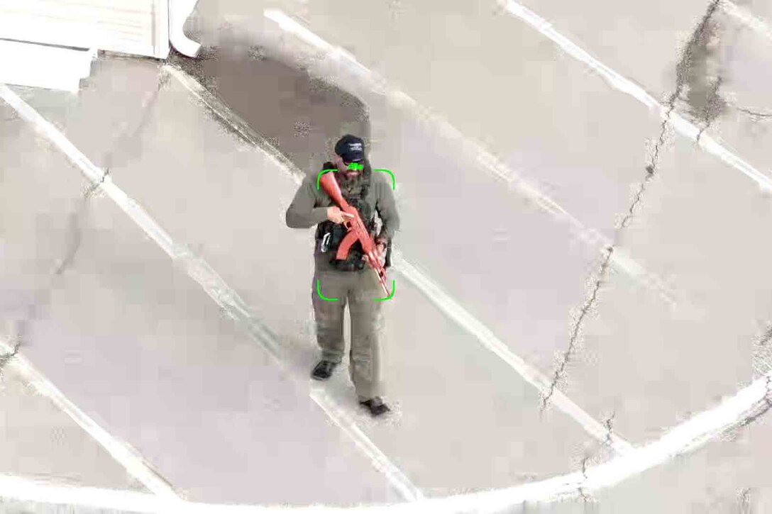 A man with an automatic rifle is highlighted by a recital on a display.