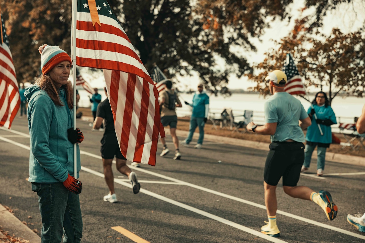 A civilian holds a flag as runners go by.