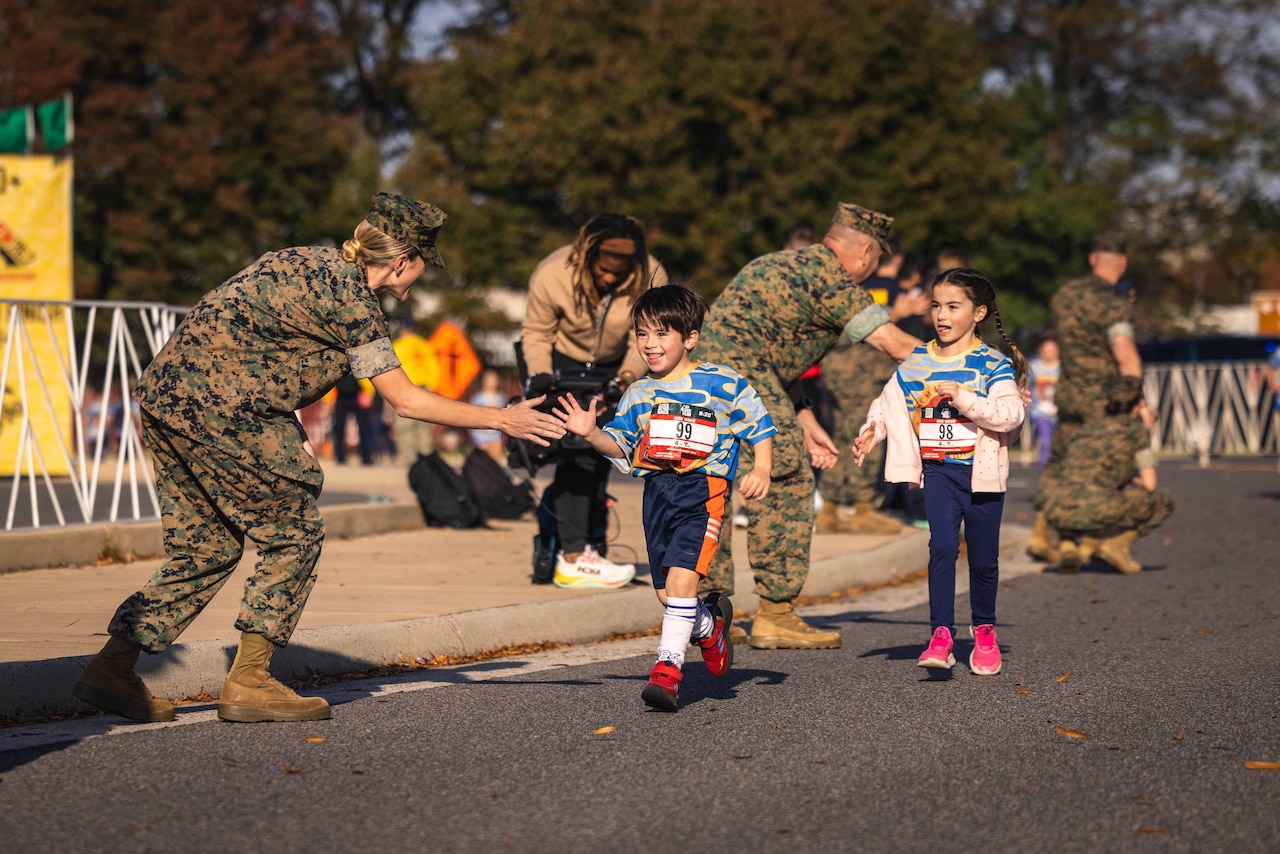 Kids get high fives from Marines as they run along a street.