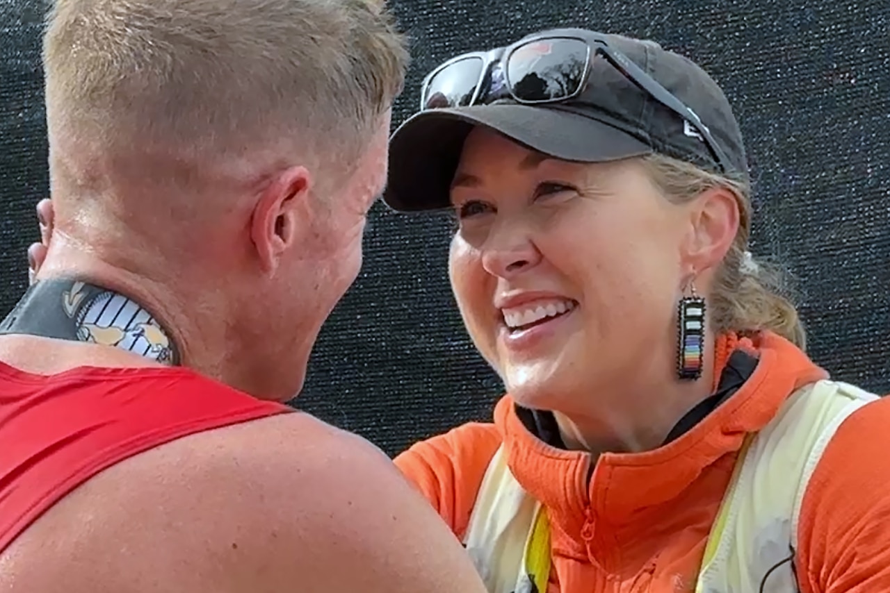 A smiling woman partially embraces a man whose face is turned from view.