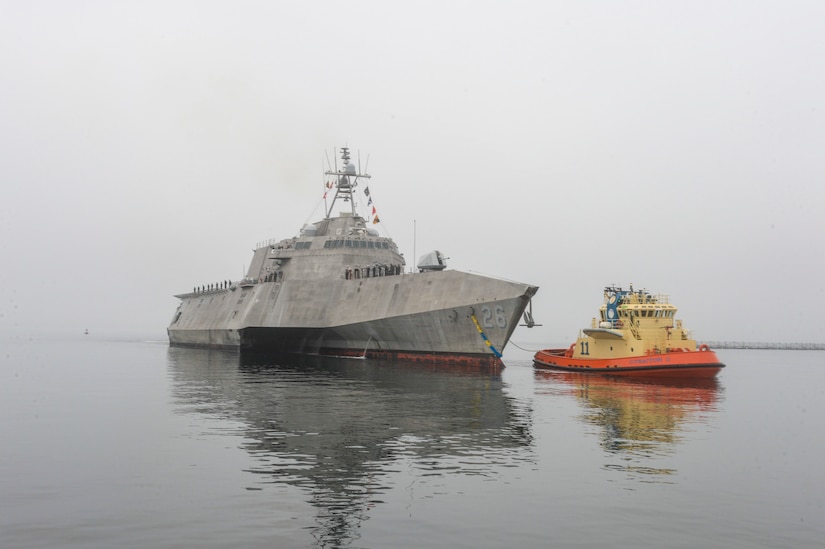 A ship and a boat sail next to each other on a gloomy day.