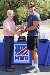 Two men stand outside holding a small trophy.