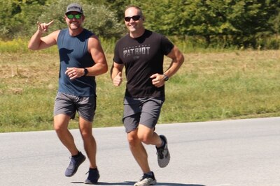 Two men in sunglasses run outside on a paved road on a sunny day.