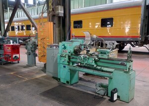 A lathe sits in a large workspace with a train car behind it.