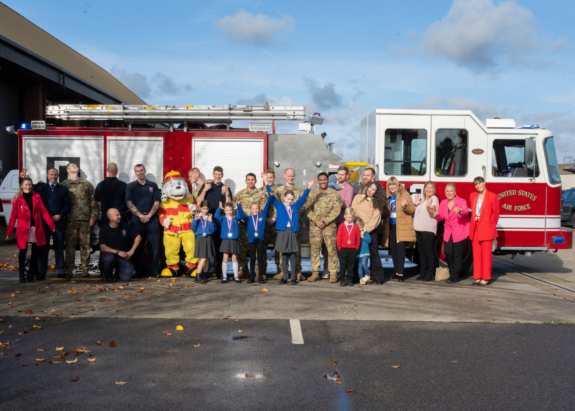 Firefighters assigned to the 100th Civil Engineer Squadron pose for a group photo with participants during the 90th birthday coloring/writing competition at Royal Air Force Mildenhall, England, Oct. 17, 2024.
