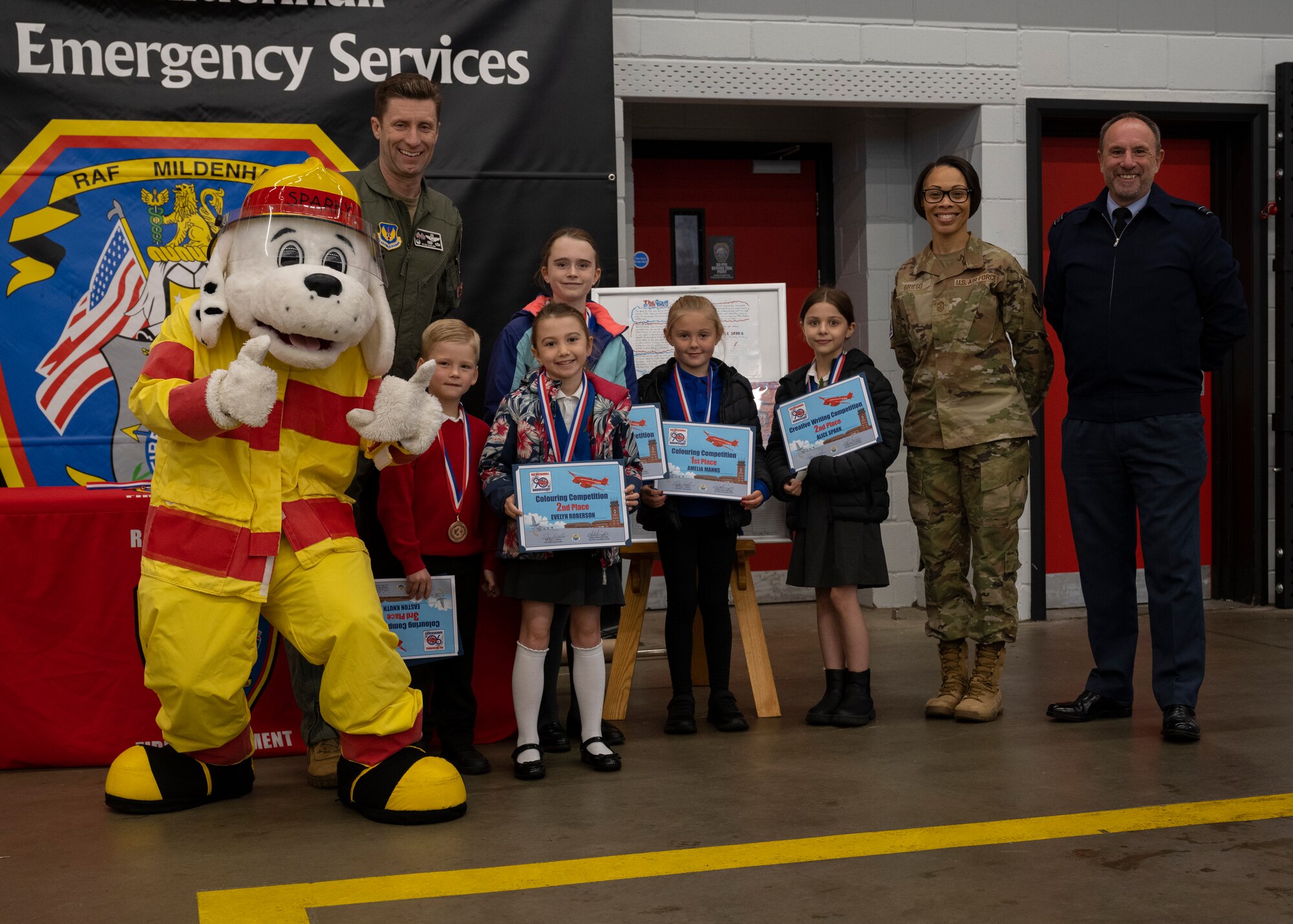 Sparky the fire dog, left, U.S. Air Force Col. Ryan Garlow, center left, 100th Air Refueling Wing commander, competition winners, center, Chief Master Sgt. Tiffany Griego, center right, 100th ARW command chief, and Royal Air Force Squadron Leader Andy Bell, right, RAF Mildenhall commander, pose for a photograph at RAF Mildenhall, England, Oct. 17, 2024.