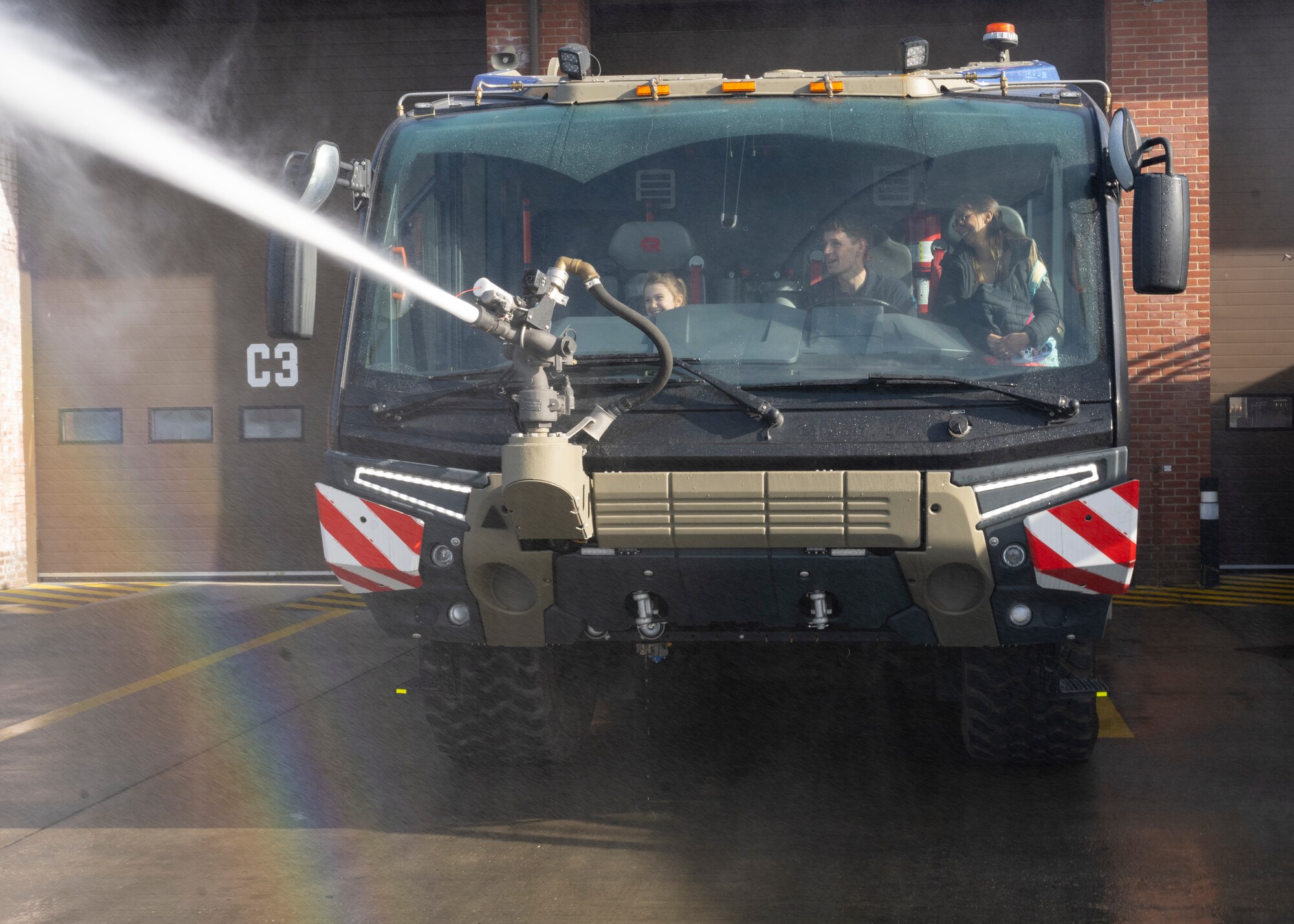 A competition winner, left, Mark Matless, center, 100th Civil Engineer Squadron Fire Department firefighter, and a guardian, right, use a fire hose during the 90th birthday coloring and writing competition at Royal Air Force Mildenhall, England, Oct. 17, 2024.