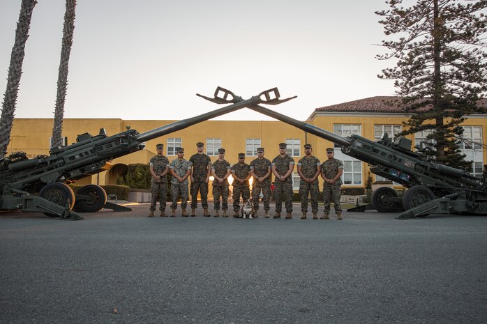 U.S. Marines with 11th Marine Regiment, 1st Marine Division, pose with Lance Cpl. Bruno, the mascot for Marine Corps Recruit Depot San Diego and Western Recruiting Region, under two M777 Howitzers at MCRD San Diego, California, Oct. 19, 2024. For the past 23 years, MCRD San Diego has hosted the Marine Corps Recruit Depot San Diego Boot Camp Challenge, a three-mile obstacle course race guided by 60 drill instructors that highlights the physical and mental demands of bootcamp. The event fosters comradery and community engagement through interaction with MCRD personnel. (U.S. Marine Corps photo by Cpl. Sarah M. Grawcock)