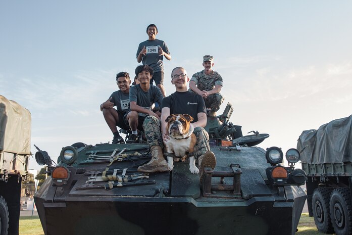 U.S. Marine Corps Cpl. Sarah Grawcock, a combat photographer and mascot handler with Headquarters and Service Battalion, Marine Corps Recruit Depot San Diego, and Lance Cpl. Bruno, the  MCRD San Diego and Western Recruiting Region mascot, pose for a photo with participants of the 2024 Marine Corps Recruit Depot San Diego Boot Camp Challenge on a Light Armored Vehicle assigned to 1st Light Armored Reconnaissance Battalion, 1st Marine Division at MCRD San Diego, California, Oct. 19, 2024. For the past 23 years, MCRD San Diego has hosted the Boot Camp Challenge, a three-mile obstacle course race guided by 60 drill instructors that highlights the physical and mental demands of bootcamp. The event fosters comradery and community engagement through interaction with MCRD personnel. (U.S. Marine Corps photo by Lance Cpl. Janell B. Alvarez)