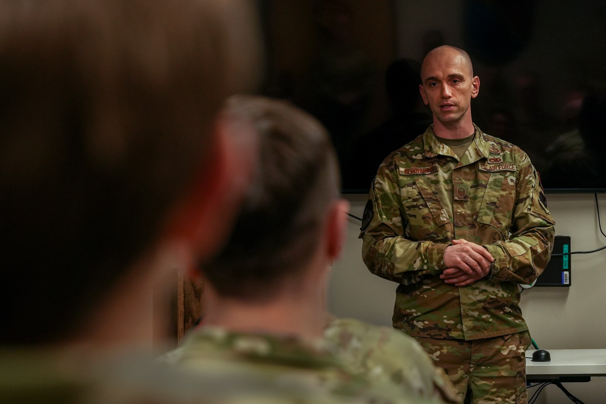 A man in a military uniform addresses a classroom of students in military uniforms.