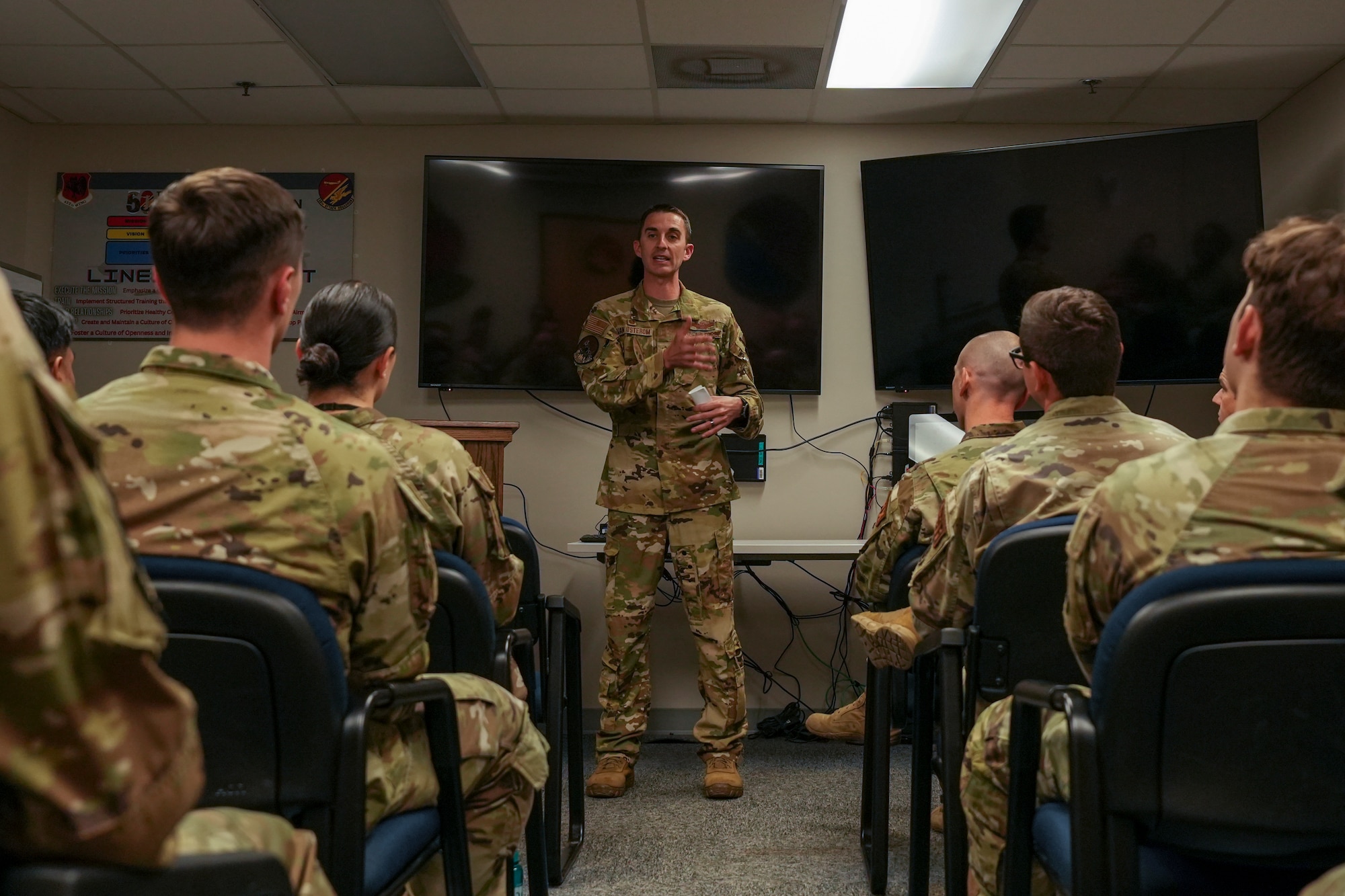 A man in a military uniform speaks to a classroom of students in military uniforms.