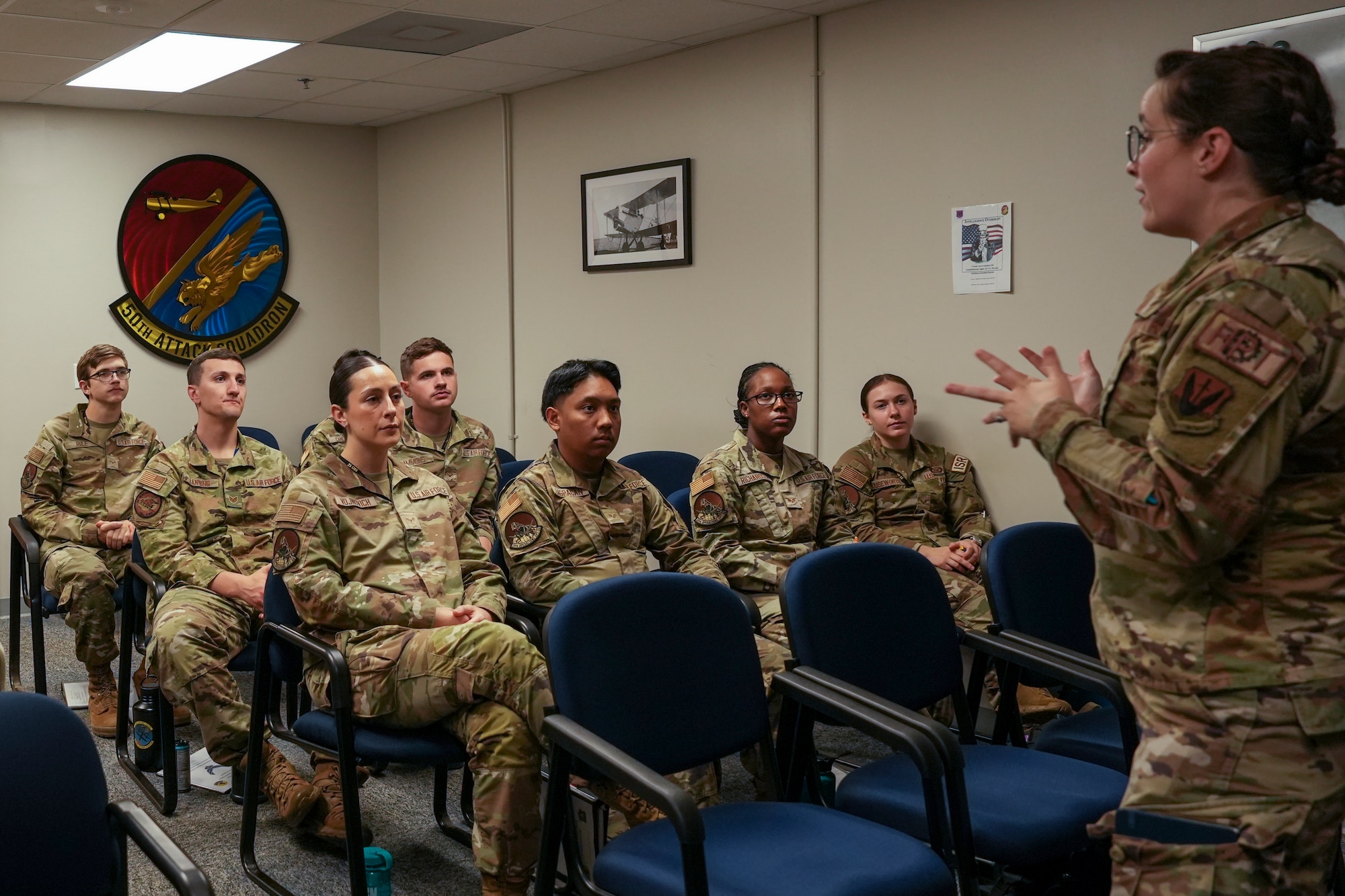 A woman in a military uniform speaks with students sitting in a classroom, also in military uniforms.