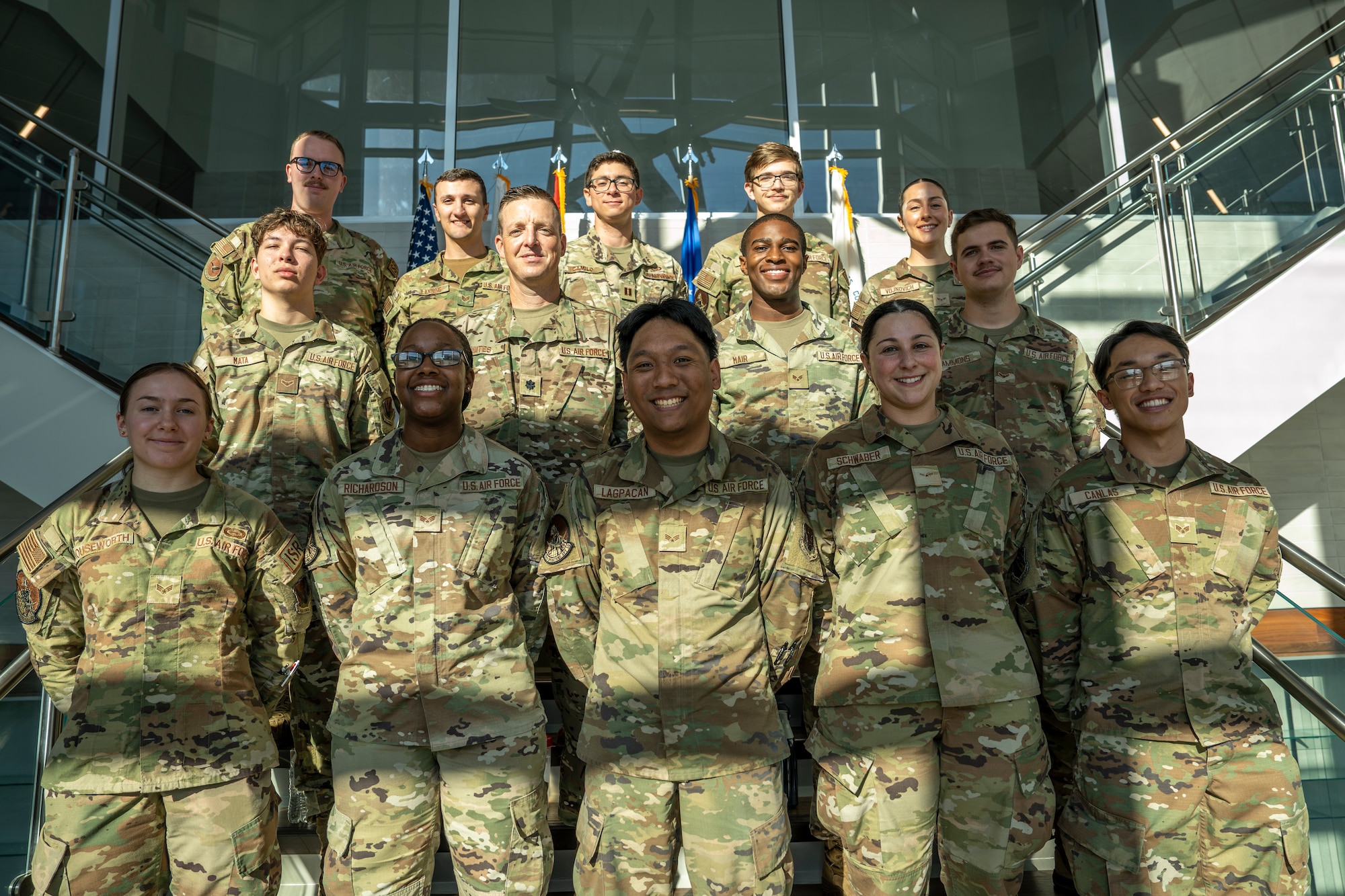 A group of men and women in military uniforms pose for a photo on a staircase.