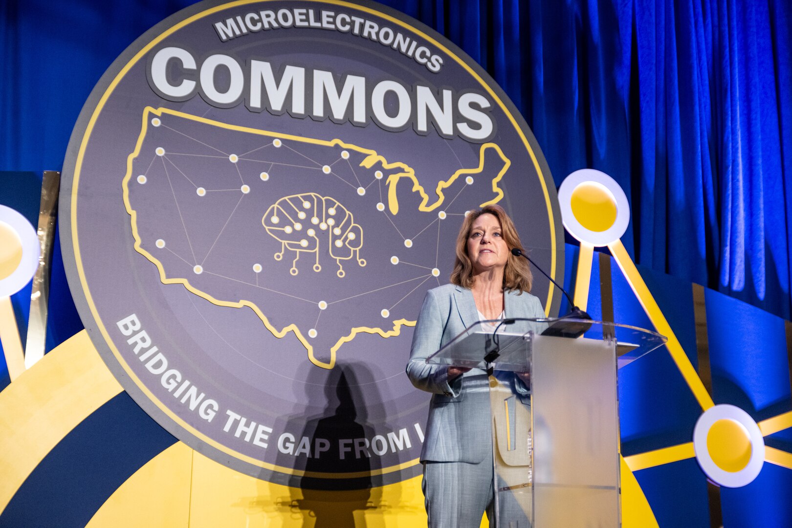 A government official delivers remarks from a podium in front of a seal with the map of the U.S. and a brain with interconnected wiring.