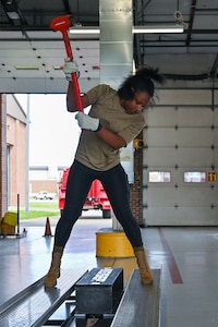 A woman in civilian clothes swings a sledge hammer