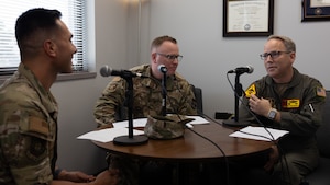 Three men sitting at table with microphones