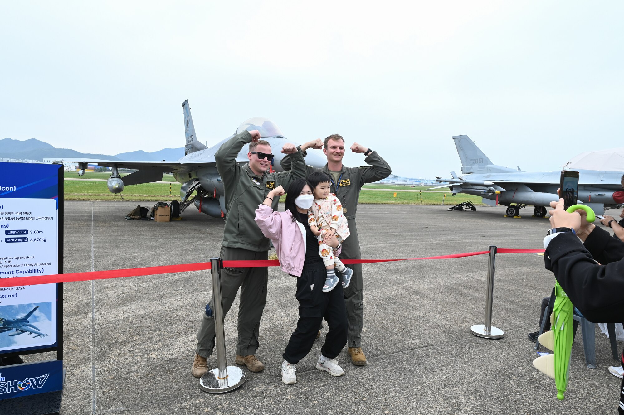 U.S. Air Force Capt. Brad Welsh and 1st Lt. Ben Evans, 80th Fighter Squadron pilots, are in flight suits, fists held above their heads, take photos with airshow-goers during the Sacheon Airshow 2024 in Gyeongnam, Republic of Korea, Oct. 27, 2024. Seventh Air Force provided an F-16 Fighting Falcon and A-10 Thunderbolt II aircraft for static displays, and participated in daily combat search and rescue demonstrations with two A-10 aircraft. (U.S. Air Force photo by Master Sgt. Rachelle Coleman)