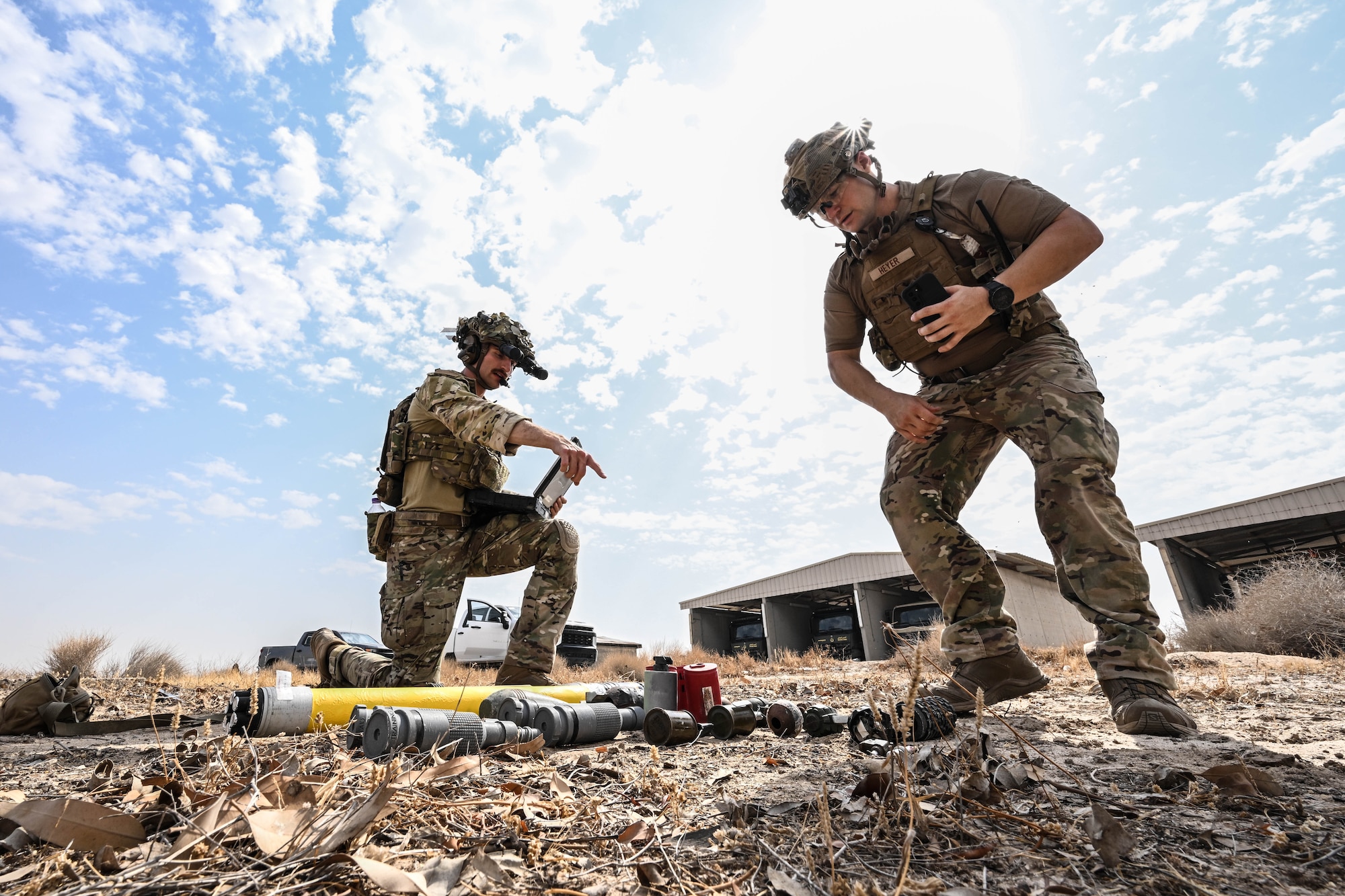 Two men in uniform look at a group of simulated explosives.