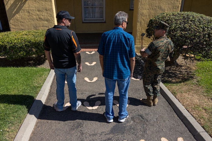 A U.S. Marine Corps drill instructor with 3rd Recruit Training Battalion, Recruit Training Regiment, Marine Corps Recruit Depot San Diego, speaks about the original yellow footprints with Terry and Dustin Bringham, the son and grandson of the late Capt. Gary L. Bringham, at MCRD San Diego, California, Oct. 21, 2024. From 1962 to 1965, Gary Bringham served as a drill instructor at MCRD San Diego before commissioning and retiring as a captain. The Bringham family toured the depot to learn more about his role as a drill instructor and the significance of training recruits. (U.S. Marine Corps photo by Cpl. Alexander O. Devereux)