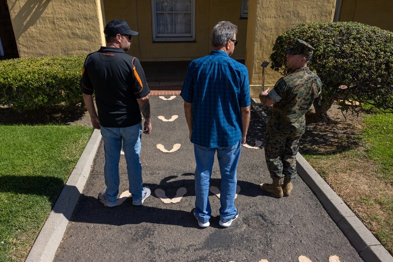 A U.S. Marine Corps drill instructor with 3rd Recruit Training Battalion, Recruit Training Regiment, Marine Corps Recruit Depot San Diego, speaks about the original yellow footprints with Terry and Dustin Bringham, the son and grandson of the late Capt. Gary L. Bringham, at MCRD San Diego, California, Oct. 21, 2024. From 1962 to 1965, Gary Bringham served as a drill instructor at MCRD San Diego before commissioning and retiring as a captain. The Bringham family toured the depot to learn more about his role as a drill instructor and the significance of training recruits. (U.S. Marine Corps photo by Cpl. Alexander O. Devereux)