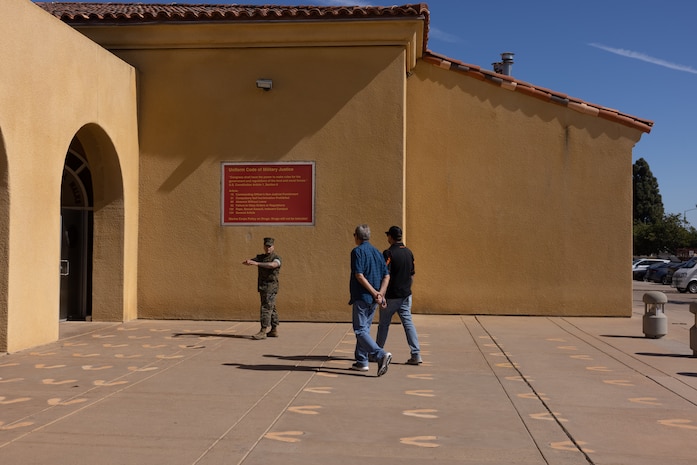 A U.S. Marine Corps drill instructor with 3rd Recruit Training Battalion, Recruit Training Regiment, Marine Corps Recruit Depot San Diego, tours the yellow footprints with Terry and Dustin Bringham, the son and grandson of the late Capt. Gary L. Bringham, at MCRD San Diego, California, Oct. 21, 2024. From 1962 to 1965, Gary Bringham served as a drill instructor at MCRD San Diego before commissioning and retiring as a captain. The Bringham family toured the depot to learn more about his role as a drill instructor and the significance of training recruits. (U.S. Marine Corps photo by Cpl. Alexander O. Devereux)
