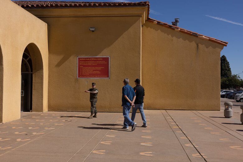 A U.S. Marine Corps drill instructor with 3rd Recruit Training Battalion, Recruit Training Regiment, Marine Corps Recruit Depot San Diego, tours the yellow footprints with Terry and Dustin Bringham, the son and grandson of the late Capt. Gary L. Bringham, at MCRD San Diego, California, Oct. 21, 2024. From 1962 to 1965, Gary Bringham served as a drill instructor at MCRD San Diego before commissioning and retiring as a captain. The Bringham family toured the depot to learn more about his role as a drill instructor and the significance of training recruits. (U.S. Marine Corps photo by Cpl. Alexander O. Devereux)