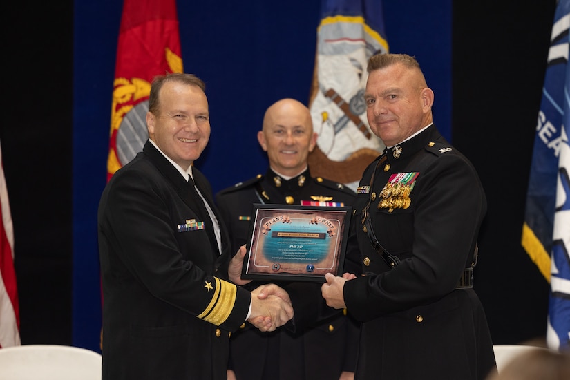 Three service members pose for a photo while holding a plaque.