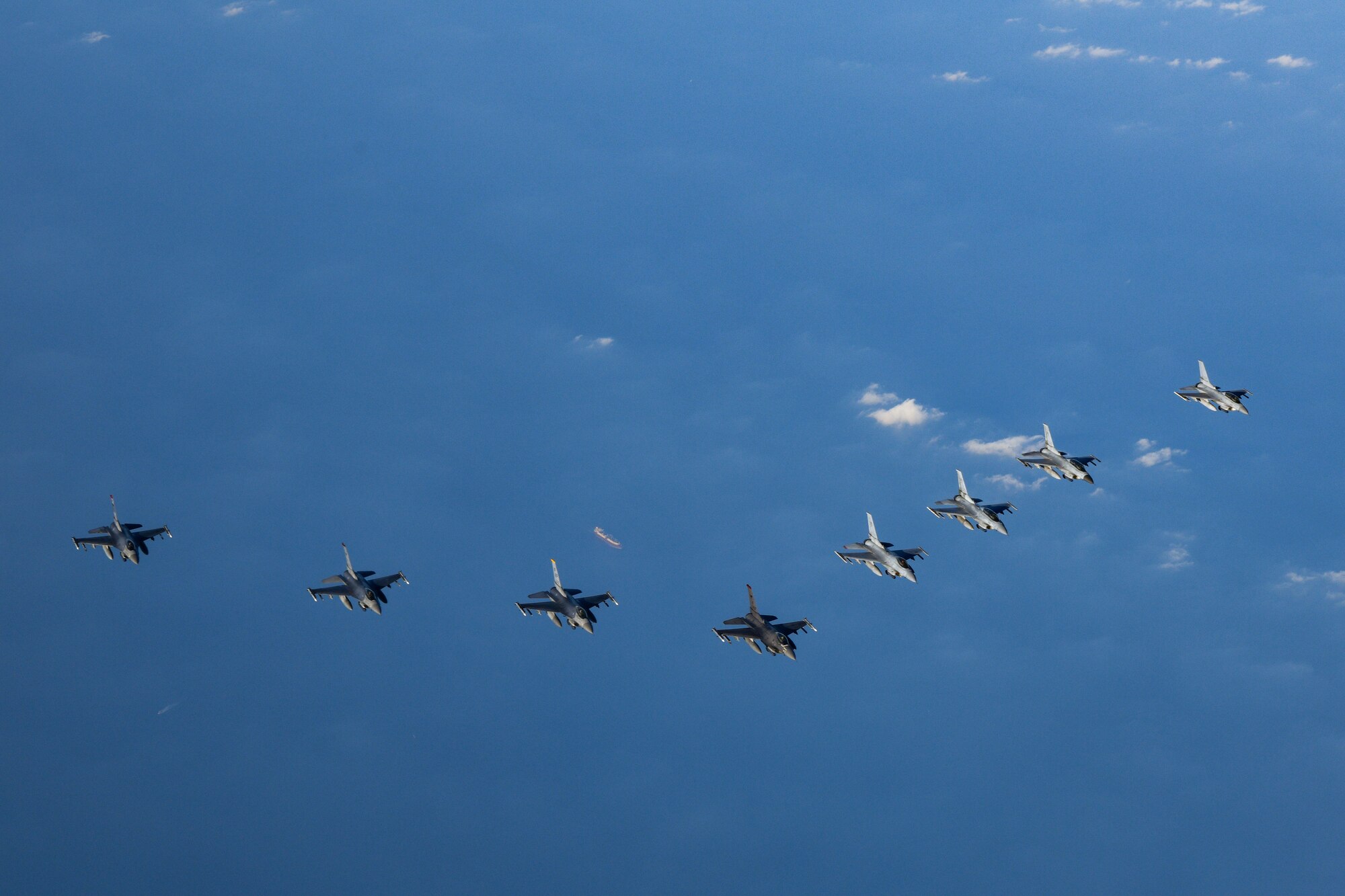 Four U.S. F-16 fighter jets flew alongside four ROK F-16 fighter jets, as seen from above, flying over blue water with clouds.
