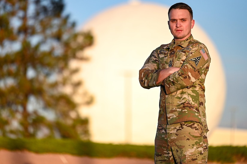 A guardian stands with arms folded in front to a radome.