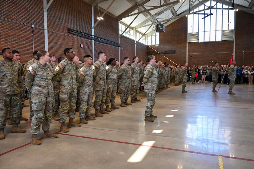 Soldiers stand in formation in a gym.