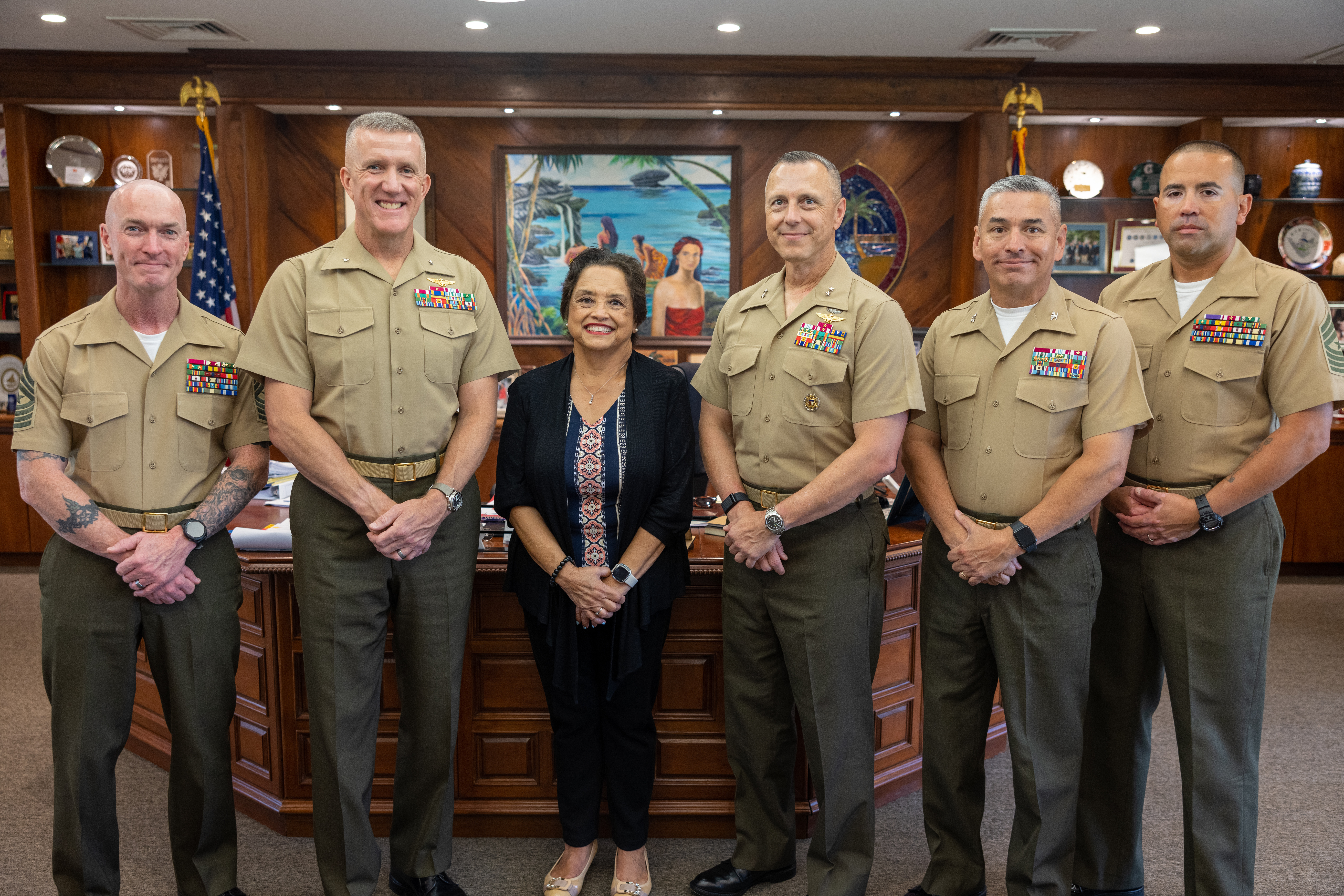 Marine Corps leaders with Honorable Gov. Lourdes Leon Guerrero, hands clasped in front of them as they smile.