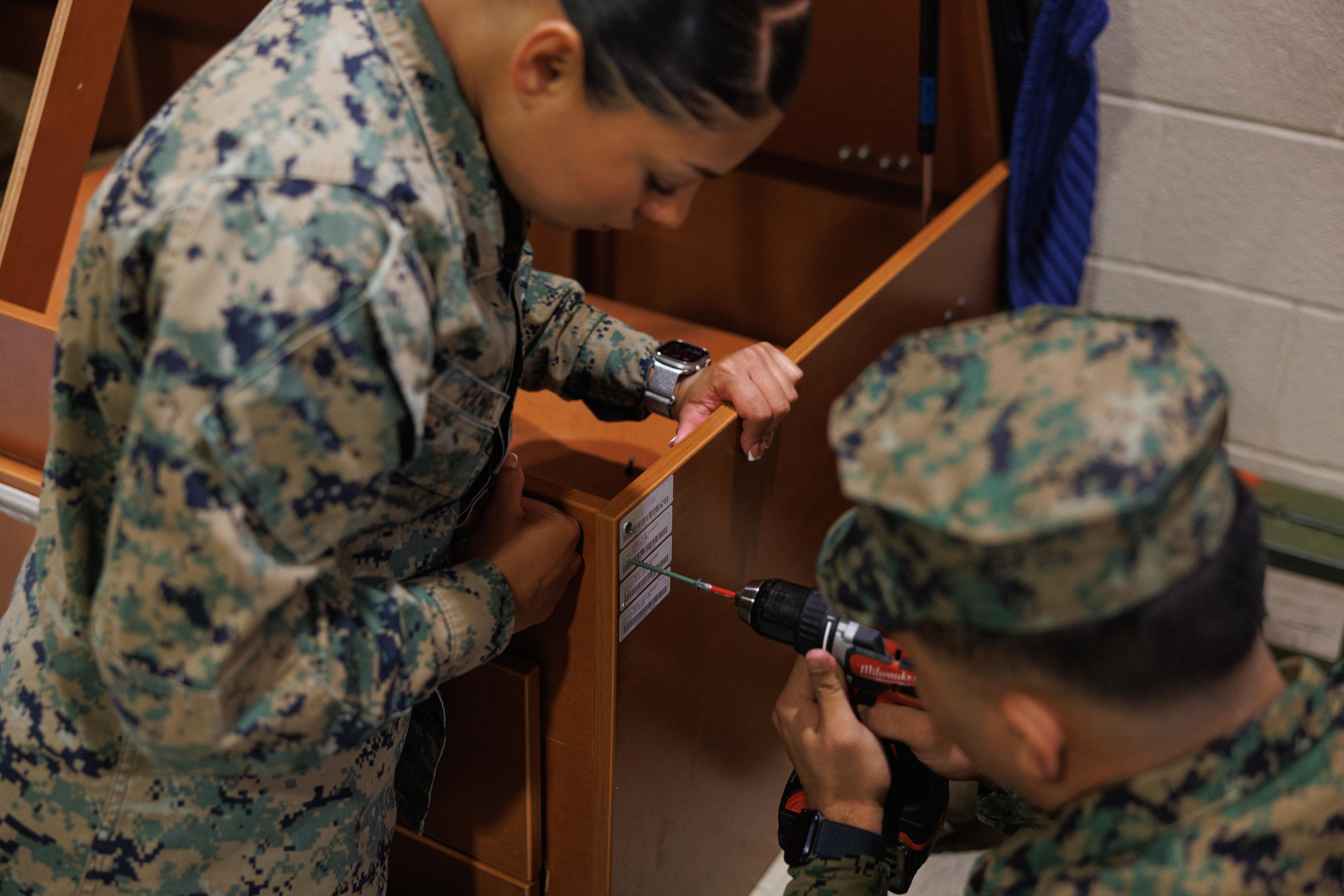Two Marines working together to build a piece of furniture in the barracks.