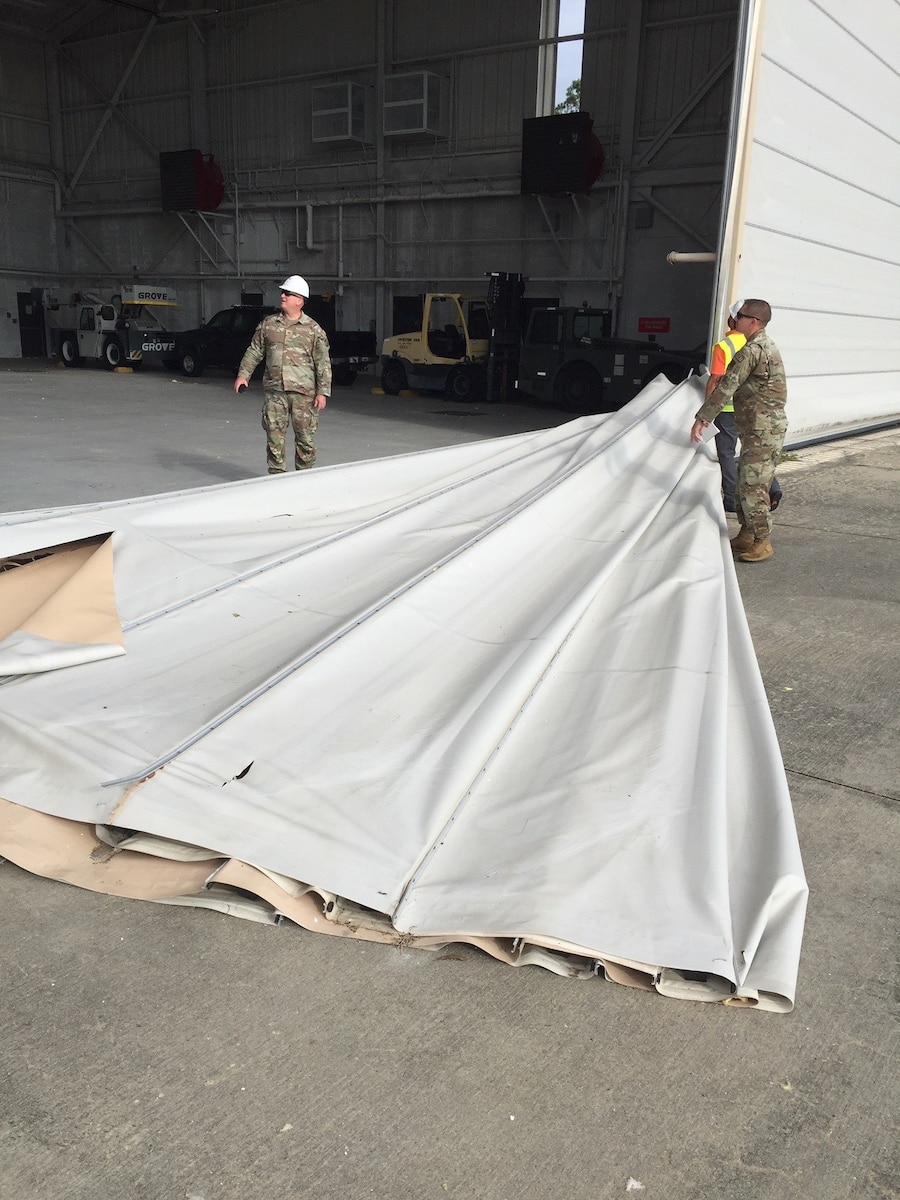 Airmen inspecting an aircraft hangar after a major storm.  One Airmen is holding a tarp from the roof.