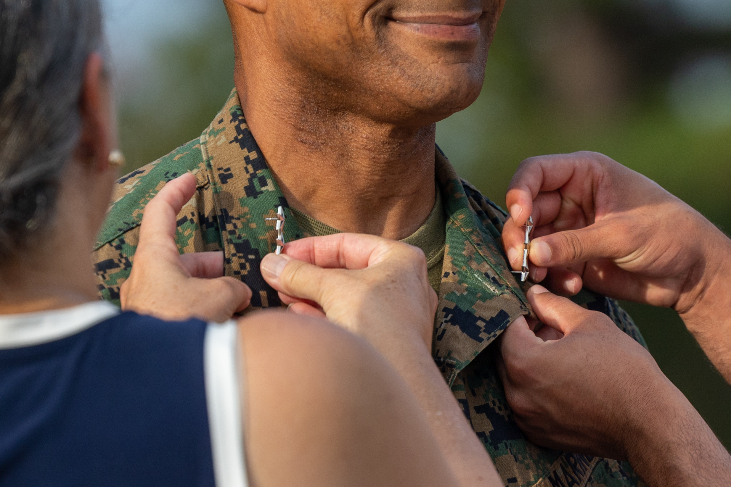 Two people pinning lapel pins on a Marine's collar.