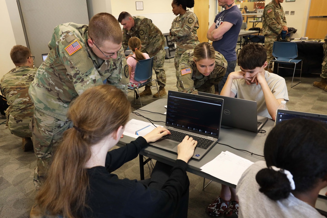 People in civilian clothing and military uniforms sit and stand around laptops.