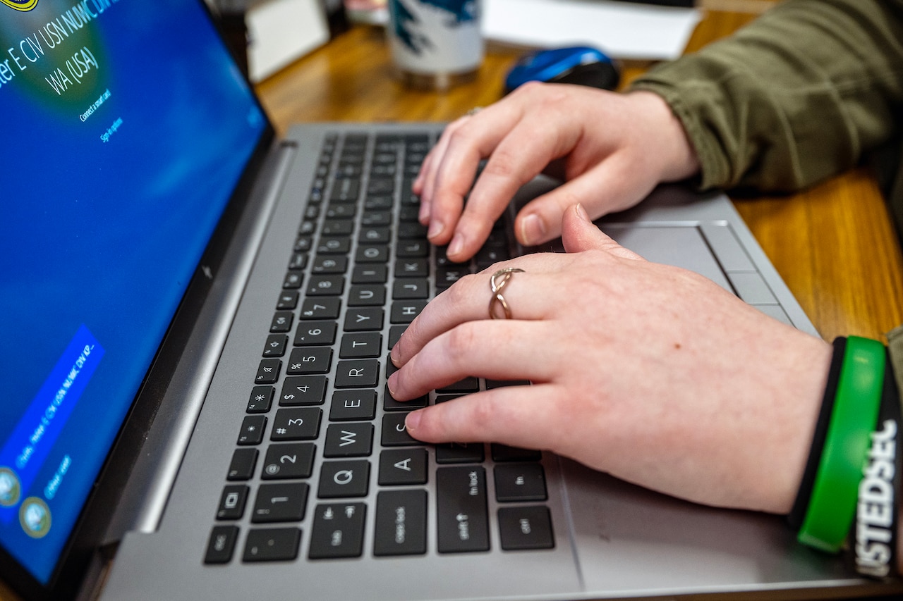 Hands type on a laptop keyboard.