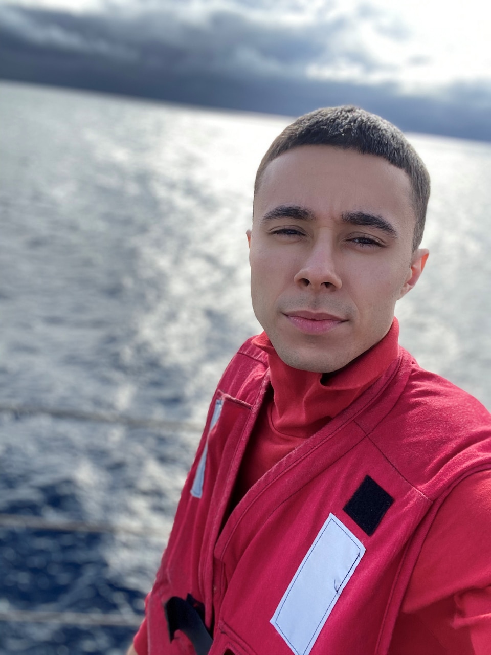 A sailor poses in uniform by the water while at sea.