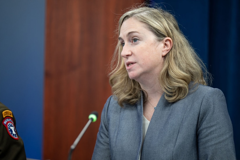 A woman in business attire is speaking into a microphone.