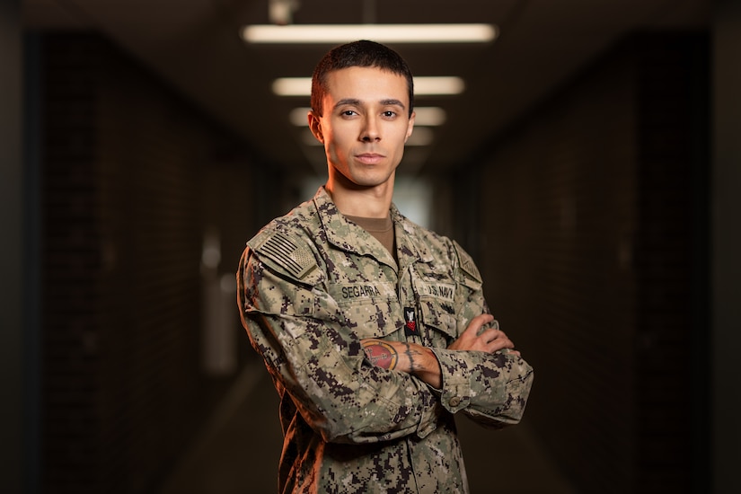 A sailor poses for a photograph in a dark hallway.